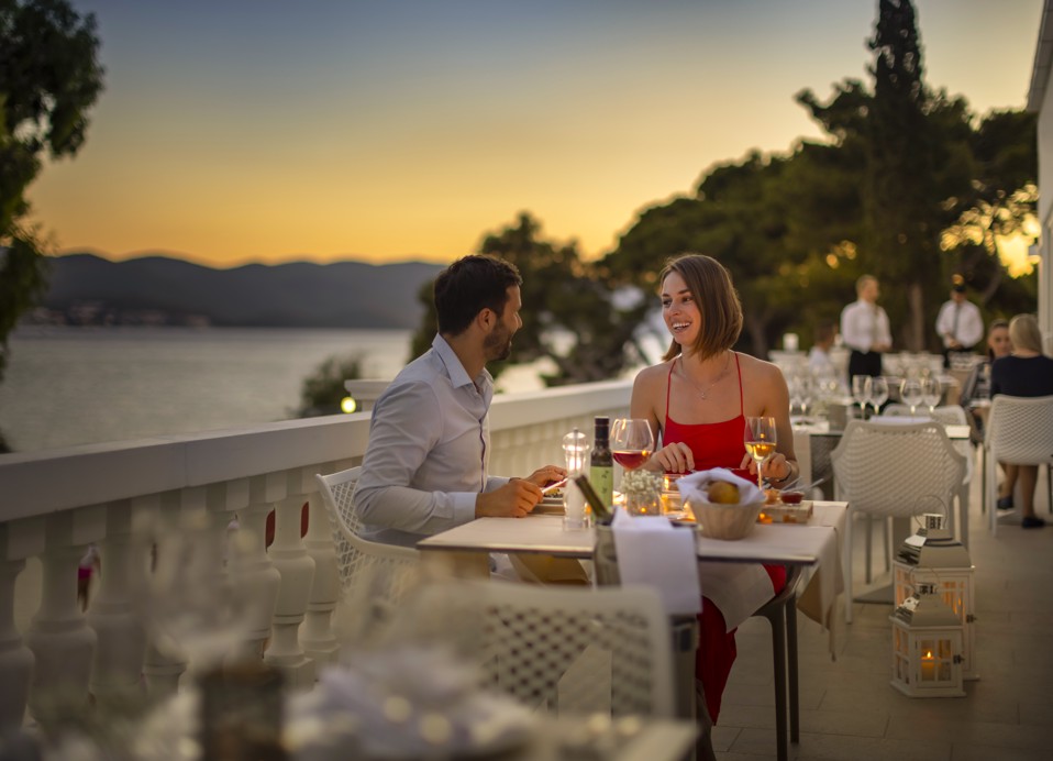Par uživa v romantični večerji ob sončnem zahodu na terasi bližnjega hotela, dostopnega gostom Aminess Maradiso Bellevue Village, s pogledom na Jadransko morje.