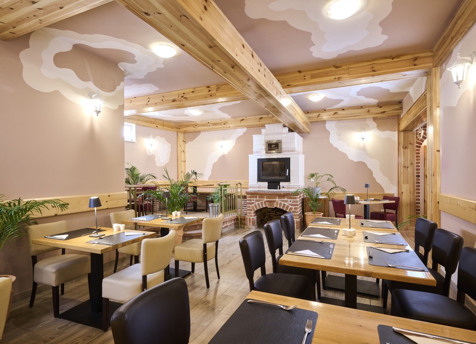 Aminess Kadoor Hotel restaurant interior with a fireplace, wooden tables and plants.