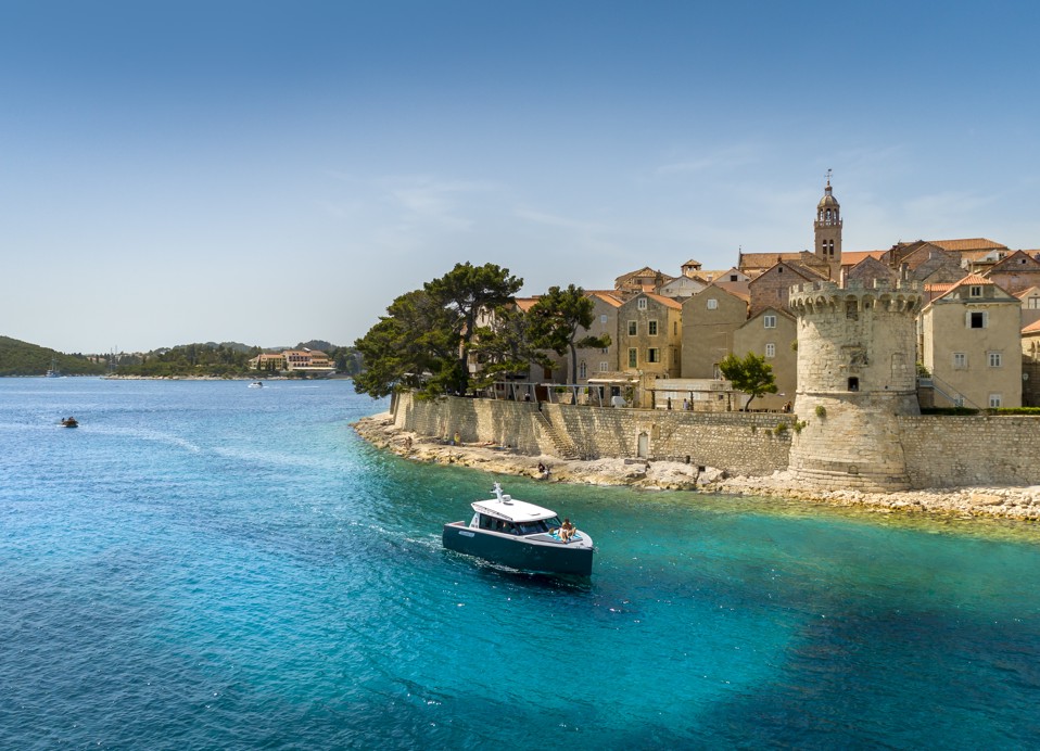 Schilderachtig uitzicht op het historische kustplaatsje Korcula, Kroatië, met een klein bootje dat de kristalheldere Adriatische Zee bevaren nabij Aminess Younique Korcula Heritage Hotel.