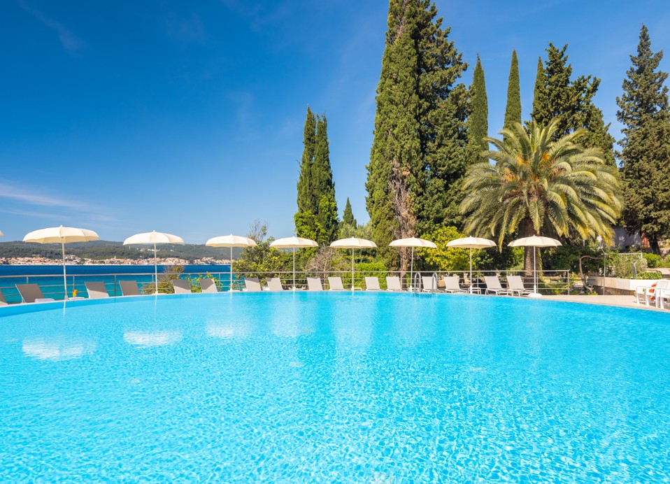 Außenpool im Orsan Maradiso Hotel by Aminess mit weißen Sonnenschirmen und Grünanlage.