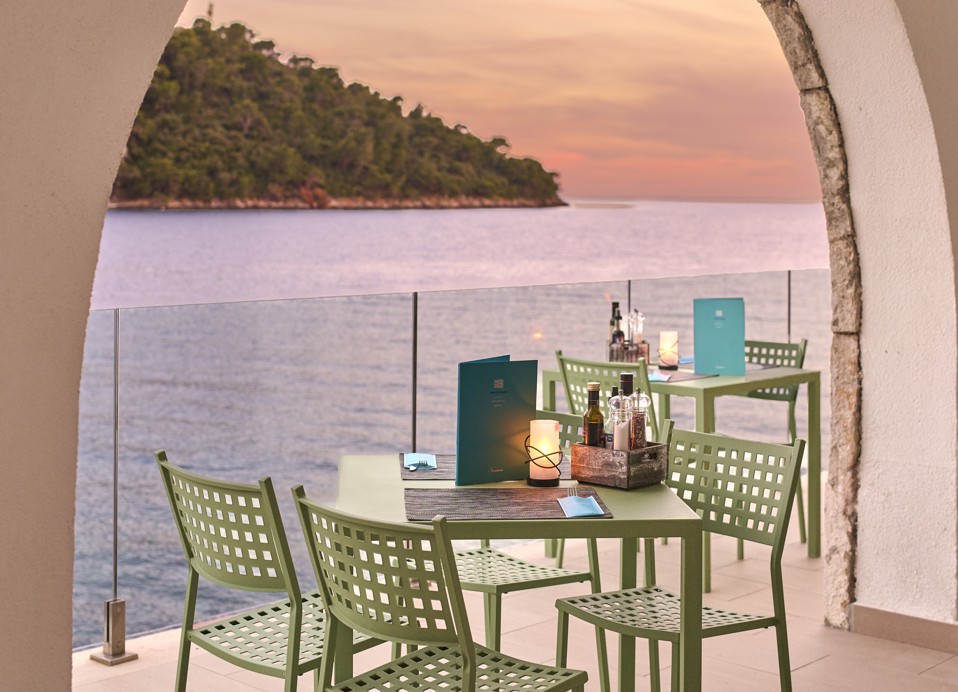 Traditionelle Adriatische Steinbogenarchitektur an der Bar des Insel-Wasserhotels, beleuchtet durch die warmen Farbtöne eines Sonnenuntergangs über dem Meer im Aminess Younique Lume Hotel.