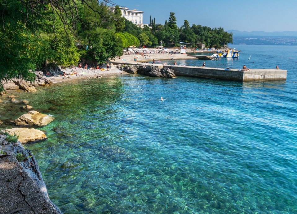 Crystal-clear sea and a rocky beach with a pier on the Opatija Riviera