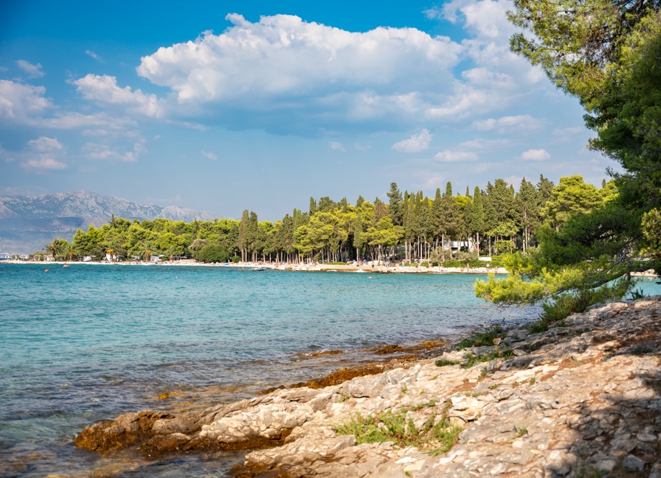 Sončna prodnata plaža s kristalno čistim morjem pred Aminess Vival Velaris Resortom na otoku Braču, popolna za poletne počitnice na Hrvaškem.