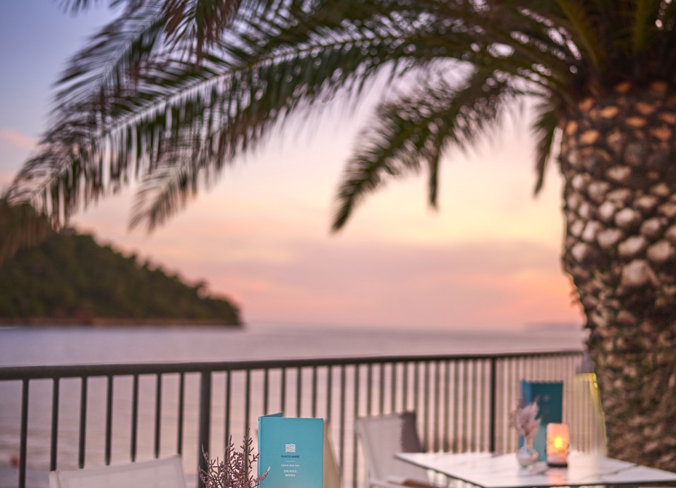 Bar im Kerzenlicht mit Blick auf das Sonnenuntergangsambiente und das beleuchtete Meer im Aminess Younique Lume Hotel.