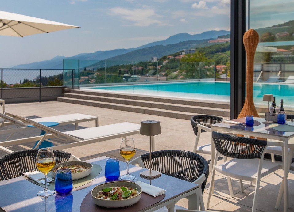 Il Cantuccio restaurant terrace by the pool with dishes and a coastal view.