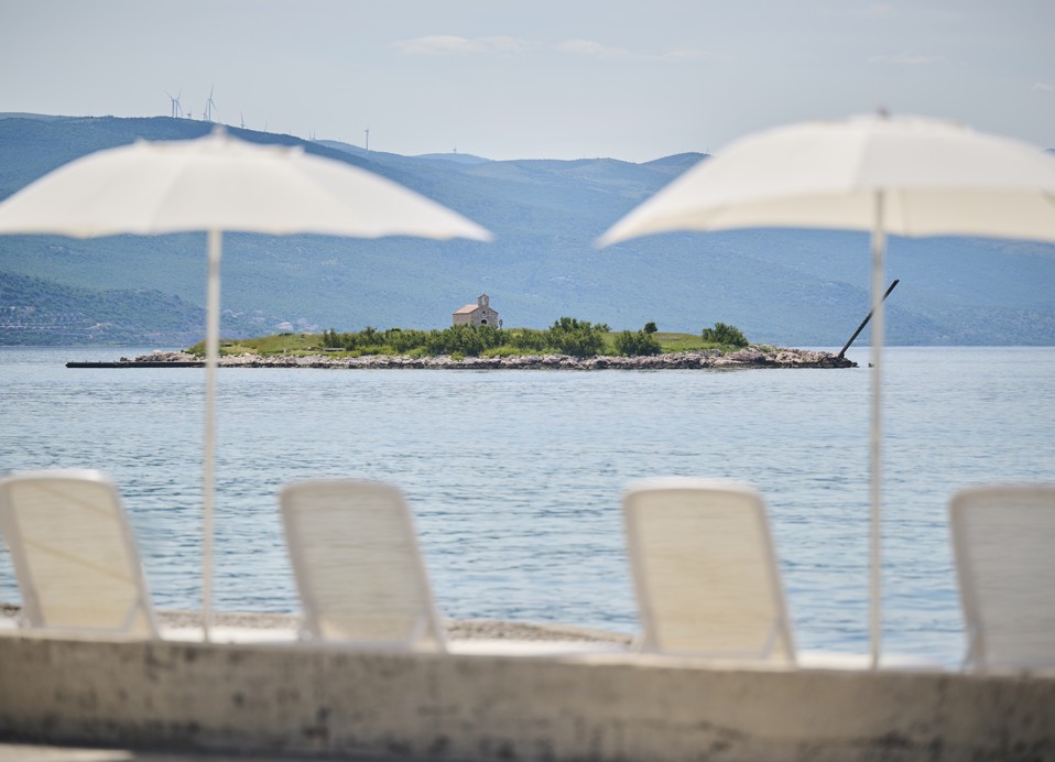 Liegestühle und Sonnenschirme am Meer mit Blick auf die Insel vor dem Hotel Aminess Lišanj.