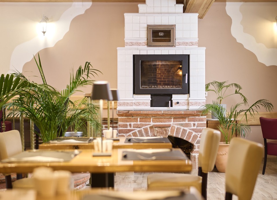 Aminess Kadoor Hotel restaurant interior with a fireplace, tables and green plants.