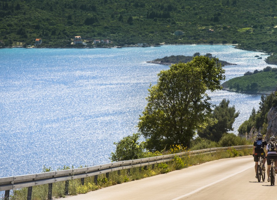 Ciklist koji vozi uz obalnu cestu s pogledom na zlatni zalazak sunca i otočni pejzaž u daljini blizu Aminess Vival Grand Azur Hotela.