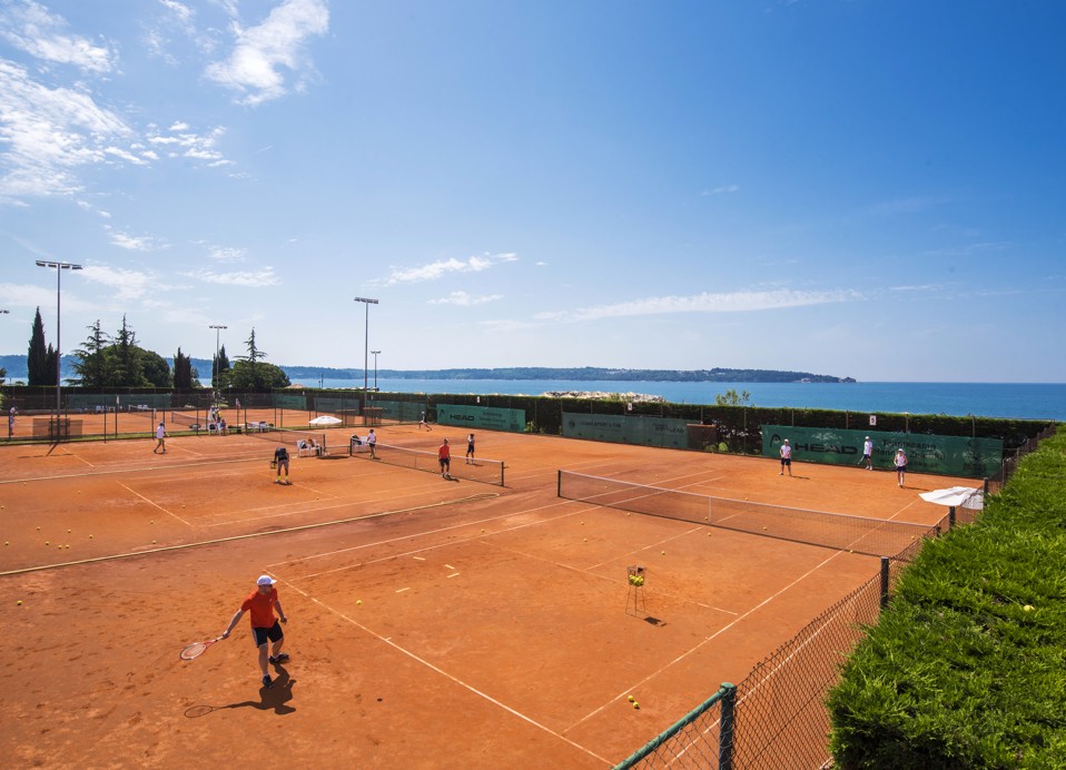 Dva teniska terena puna igrača, s pogledom na more u pozadini.