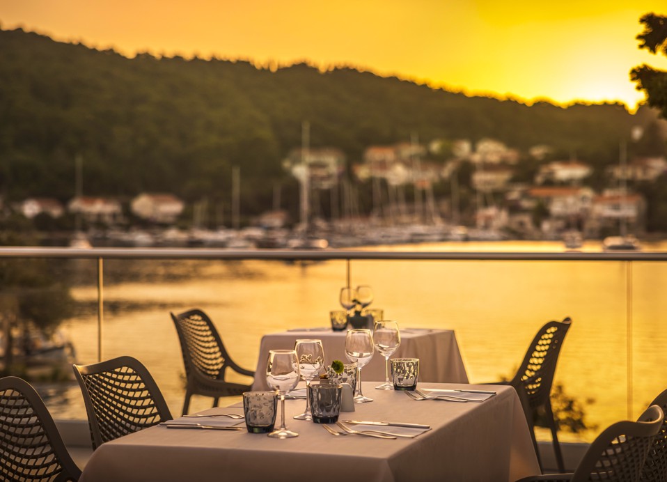 Stol postavljen s tanjurima, priborom za jelo i čašama na terasi unutar resorta, blizu Port9 Planet Camping by Aminess.