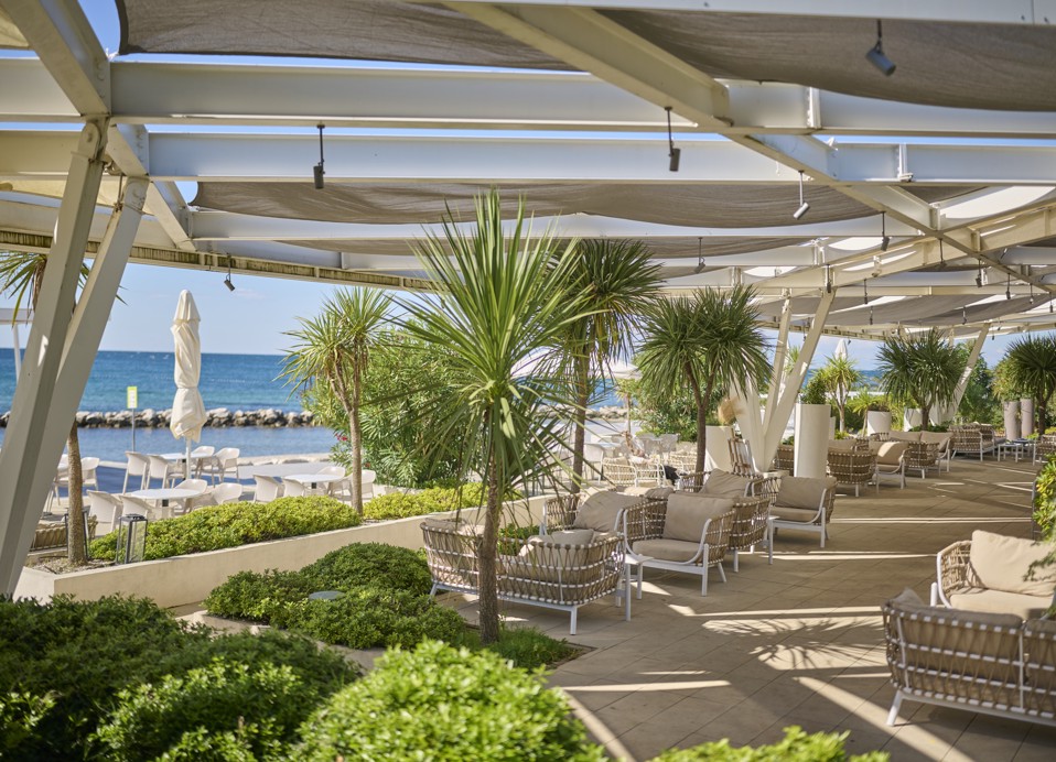 Vista sulla spiaggia dall’area ombreggiata del ristorante presso Aminess Planet Camping Maravea Resort, con case mobili e spazi verdi visibili, luogo perfetto per rilassarsi e gustare un pasto