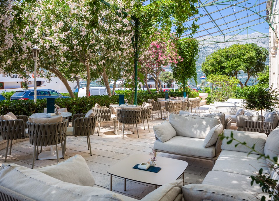 Esterno del terrazzo del lounge bar G&T all'interno dell'Aminess Korcula Heritage Hotel, con eleganti divani lounge, lussureggiante vegetazione di piante mediterranee come l'oleandro.