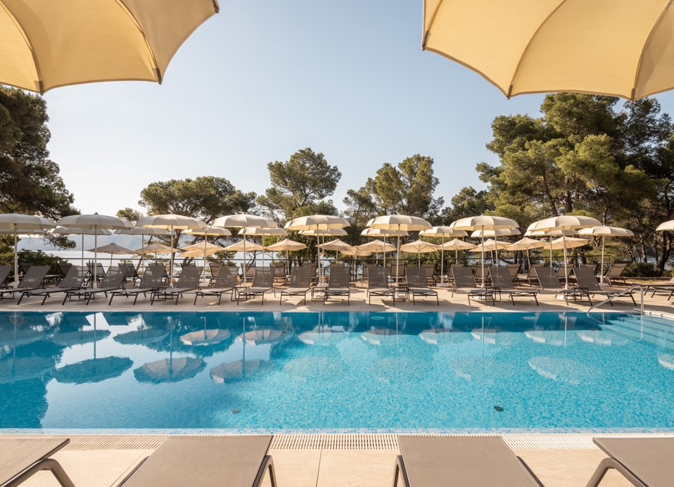 Outdoor pool with sun loungers and parasols surrounded by pine trees at Aminess Younique Senses Resort on Hvar island