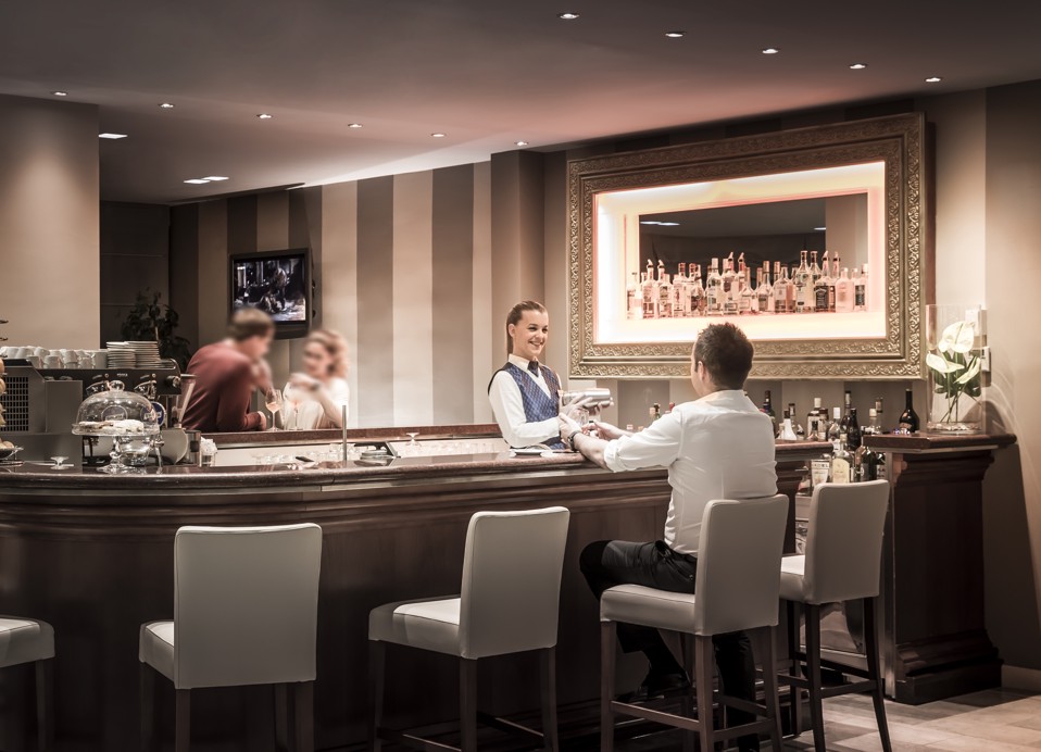 Innenansicht einer stilvollen Hotellobby-Bar mit Gästen, die Getränke an der Theke im Aminess Vival Grand Azur Hotel genießen.