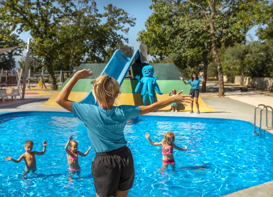 Kinder genießen Wasserspiele, angeleitet von einem Animator, in einem lebhaften Poolbereich im Aminess Style Camping Atea Resort.