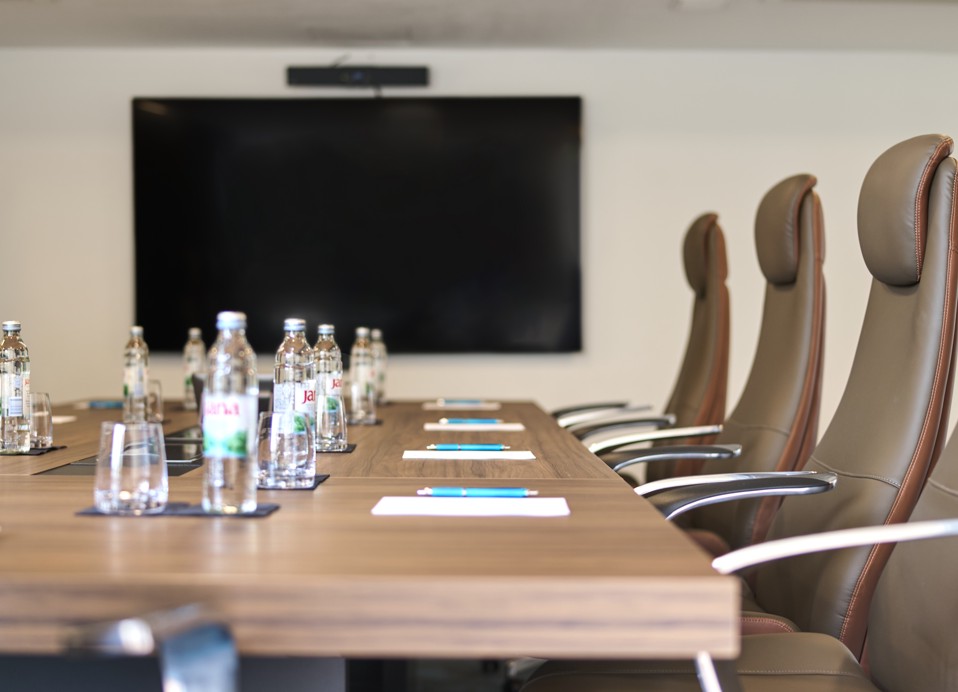 The image shows a meeting table setup, with water, a notepad, and a TV.