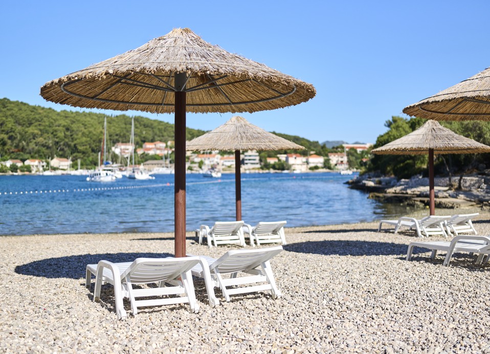 Slamnate senčnice in ležalniki na prodnati plaži pri Port9 Planet Camping by Aminess, Korčula.