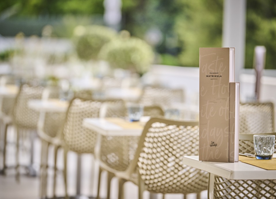 Moderan stol postavljen s jelovnikom a la carte ponude na terasi restorana Matrikula unutar resorta, blizu Port9 Planet Camping by Aminess.