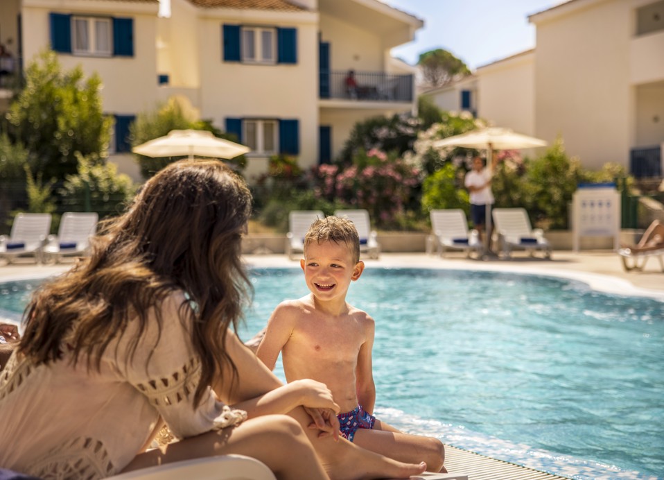 Bambini che si divertono nella piscina disponibile per le holiday home a Port9 Planet Camping by Aminess, circondati da palme e sedie a sdraio.