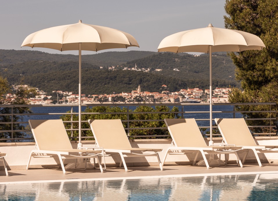 Sonnenliegen und Sonnenschirme am Pool des Aminess Bellevue Hotels in Orebić mit Blick auf das Meer und Korčula