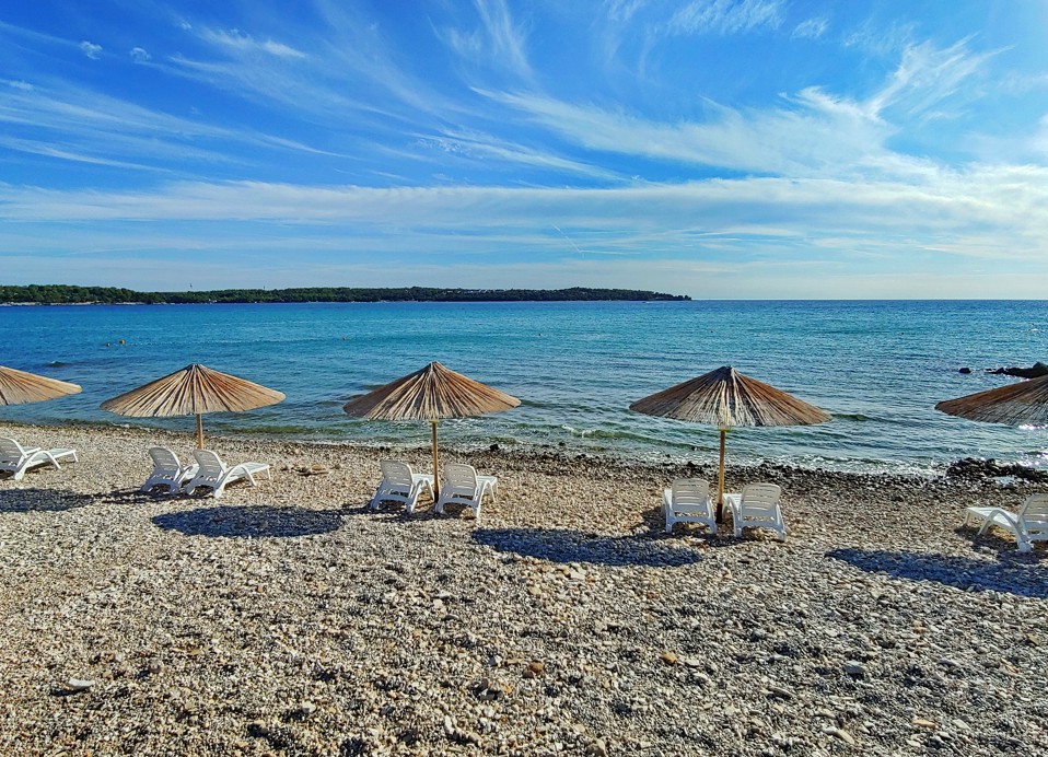Spiaggia di ciottoli con ombrelloni presso Aminess Planet Camping Sirena a Novigrad, Croazia