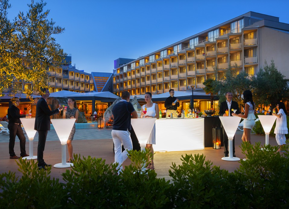 Evenement op het buitenterras van het hotel bij de poolbar, met nachtverlichting en mensen die van cocktails genieten.