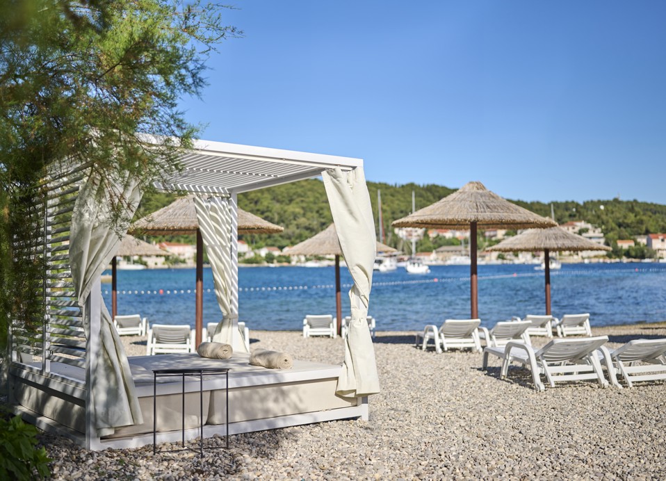 Ein Himmelbett am Kieselstrand, das einen gemütlichen Ort zum Entspannen und Genießen des Meerblicks im Aminess Vival Port9 Resort in Korcula bietet.