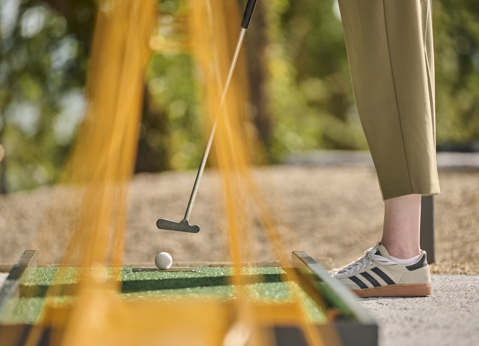 Persoon speelt minigolf en maakt zich klaar om de bal te slaan met een putter op een buitenterrein.