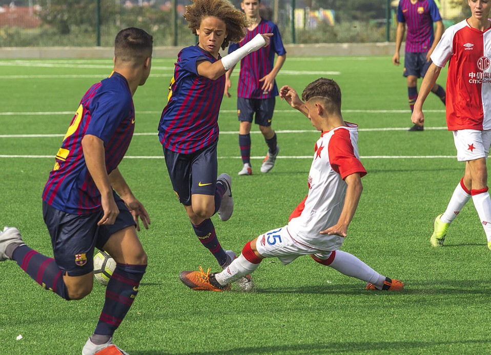 Junge Fußballer, die während eines Spiels auf einem grünen Kunstrasenplatz um den Ball kämpfen.