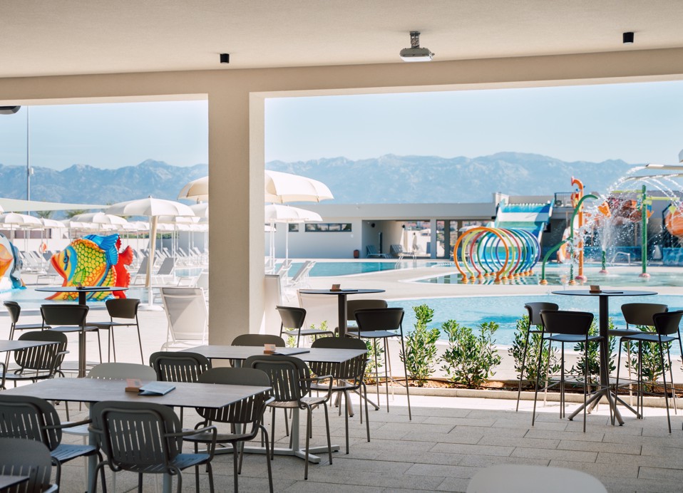 Terras van de bar met tafels en stoelen, uitzicht op het Aquapark in Aminess Style Camping Avalona resort.