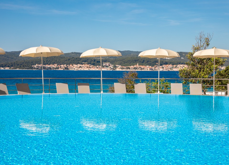 Pool im Orsan Maradiso Hotel by Aminess mit Sonnenschirmen und Meerblick.