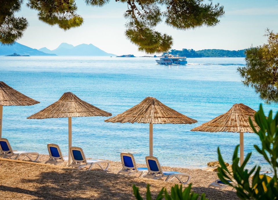 Blick auf den Strand mit Sonnenschirmen und Liegen vor dem Aminess Vival Grand Azur Hotel, Orebić.