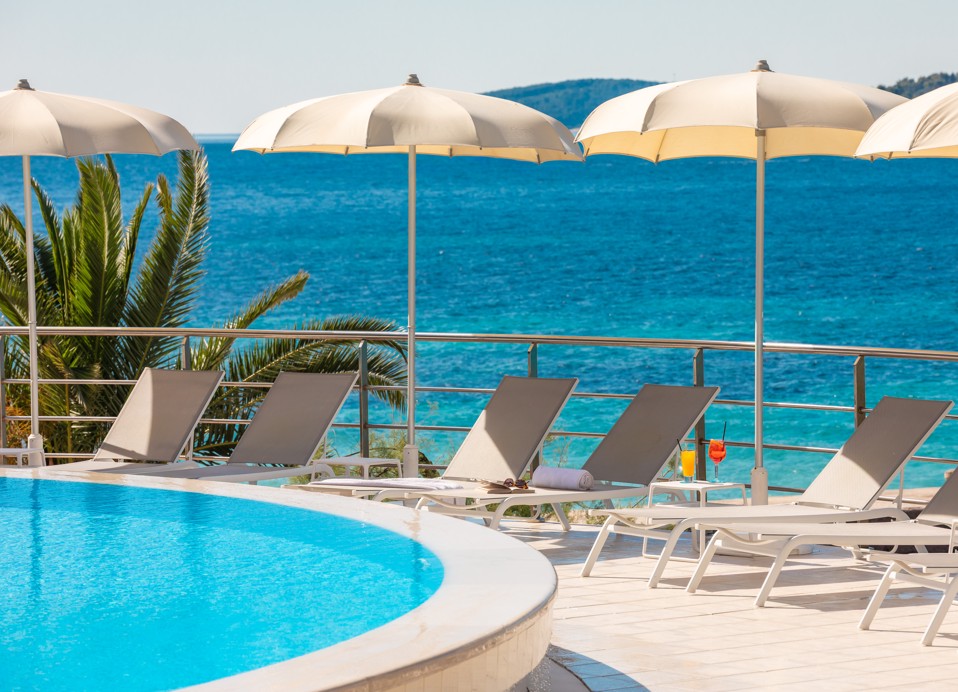 Pool im Orsan Maradiso Hotel by Aminess mit Liegen, Sonnenschirmen und Meerblick.