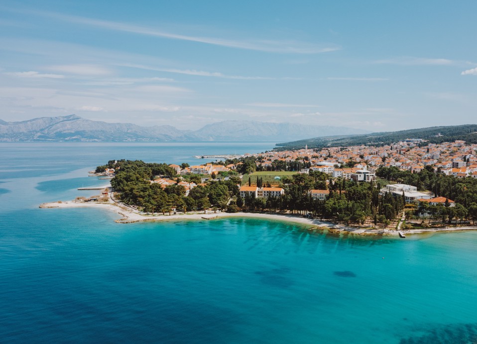 Zračni pogled na turkizno morje, plažo in mesto ob Aminess Vival Velaris Resort na otoku Braču – popolna destinacija za poletne počitnice na Hrvaškem.