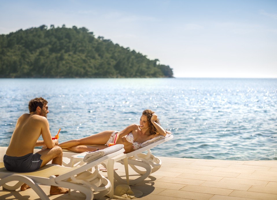 Couple sunbathing on the beach loungers next to the crystal clear Adriatic sea on the island of Korcula at Aminess Younique Lume Hotel.