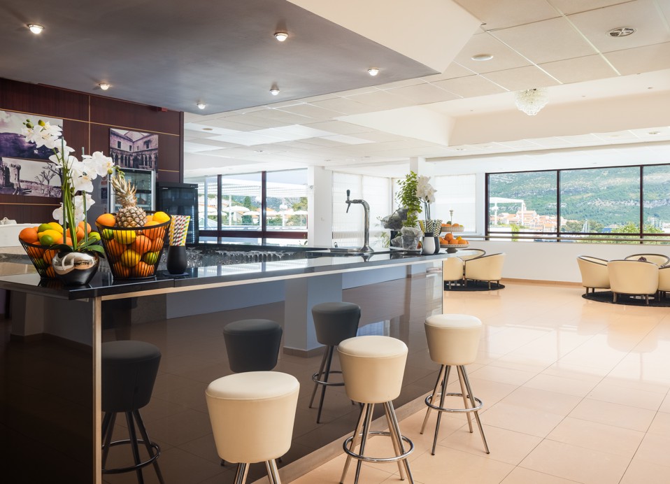 Modern aperitif bar at the Maradiso Marko Polo Hotel by Aminess, with sleek decor including white bar stools, polished dark wood counters, and panoramic windows showcasing the outdoor surroundings.