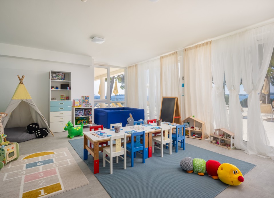 Mini club playroom at Younique Bellevue Hotel with tables, toys and a plush caterpillar.