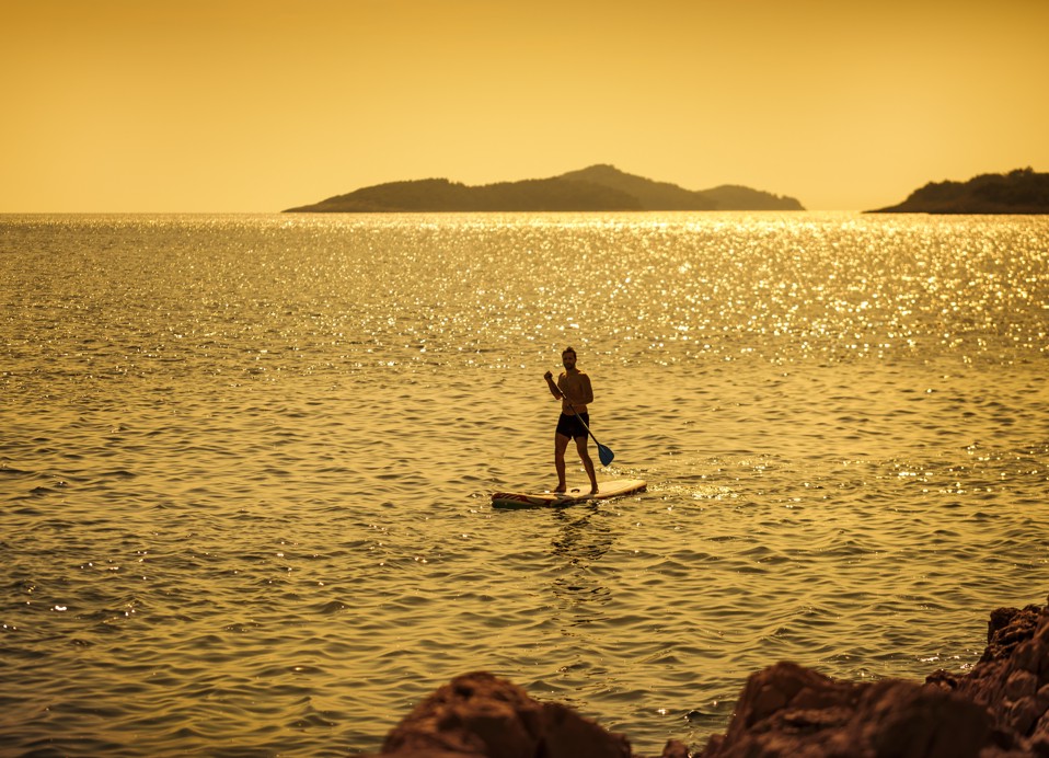 Muškarac na dasci za veslanje na mirnom moru, okupan toplim sjajem zalaska sunca, uživa u večernjoj mirnoj vježbi blizu Aminess Younique Lume Hotela.