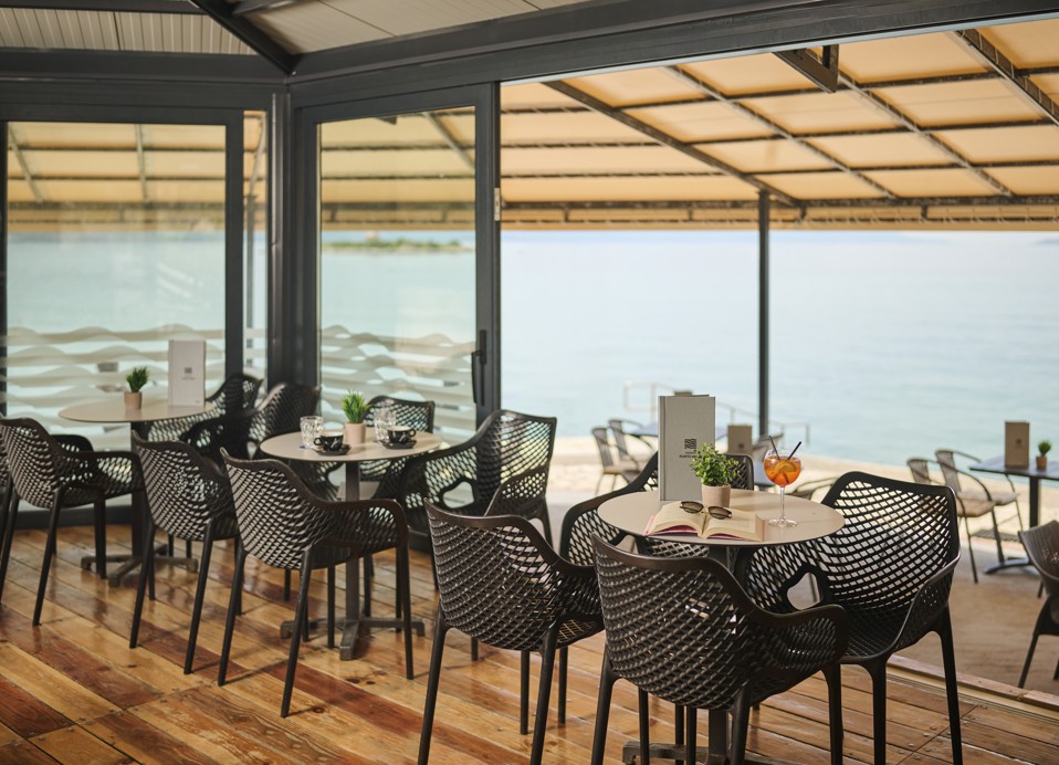 Pokrita terasa beach bara ob morju s pogrnjenimi mizami in pijačo, hotel Aminess Lišanj.