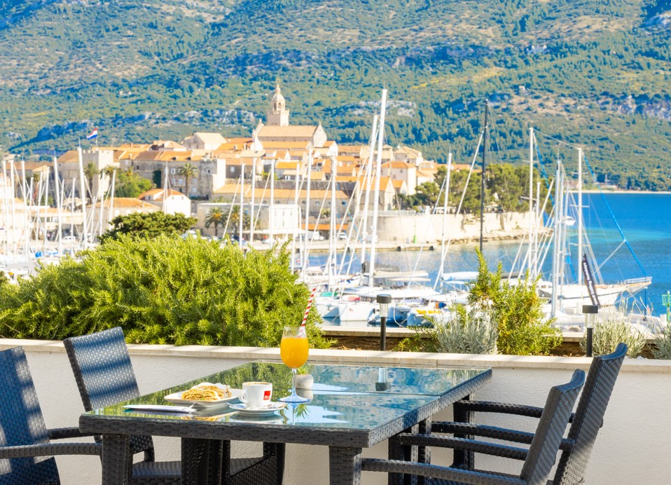 Pool bar at Maradiso Marko Polo by Aminess in Korcula with an elevated view of the marina, red-roofed town buildings, and lush greenery.