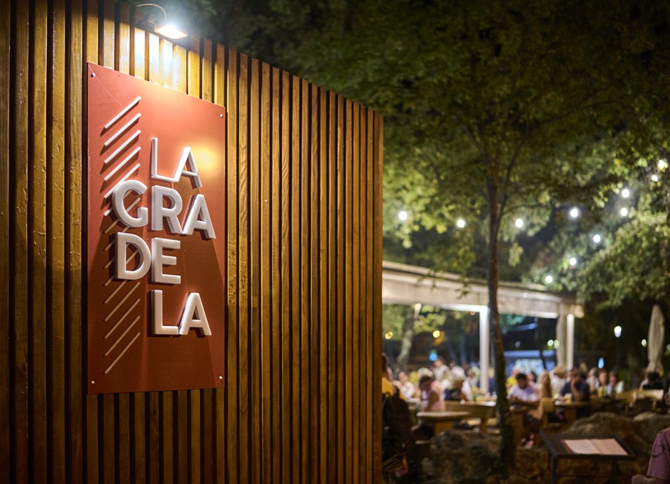 Večerna atmosfera v restavraciji La Gradela z toplim razsvetljavo, lesenim zunanjim delom in živahnim zunanjim jedilnim prostorom, obdanim z drevesi, blizu Aminess Style Camping Atea Resort.