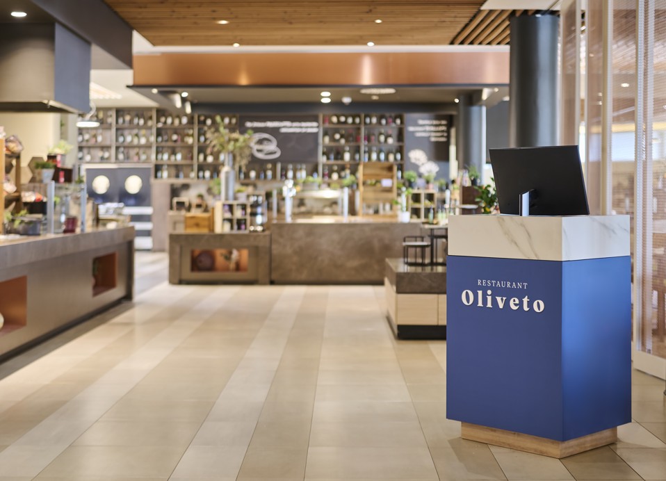 De afbeelding toont de restaurantmanager bij de receptie met mensen op de achtergrond.