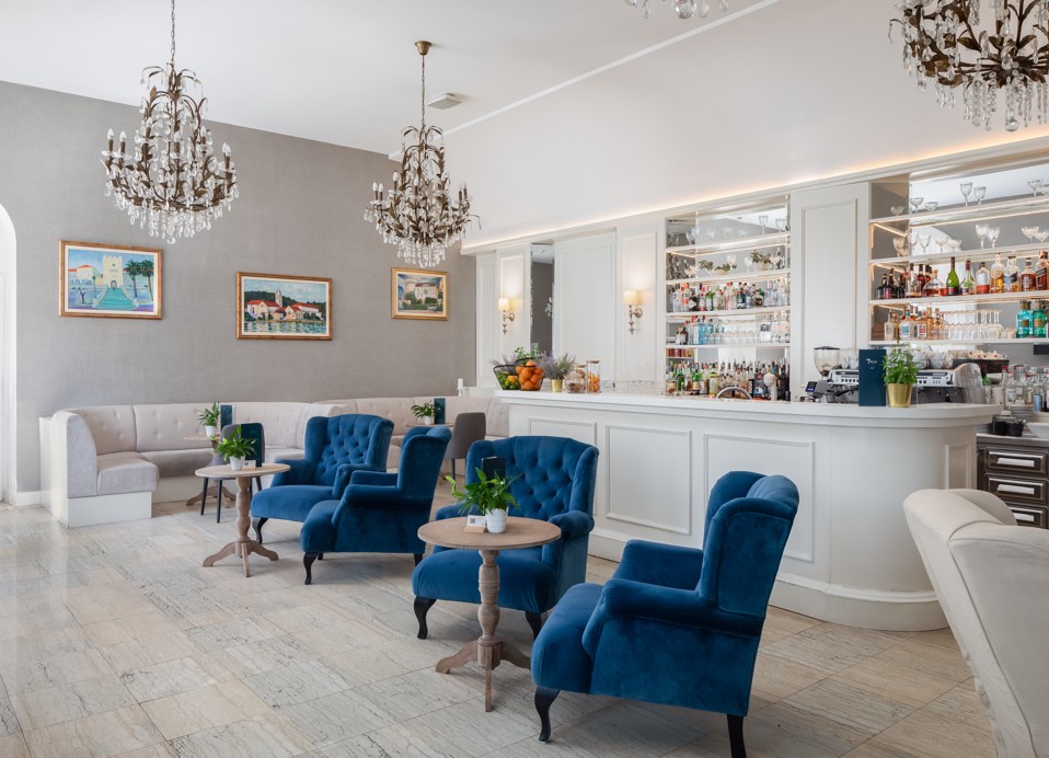 Interno del bar lounge G&T all'interno dell'Aminess Korcula Heritage Hotel, con un elegante arredamento blu e grigio, poltrone lounge blu e un lampadario di cristallo.