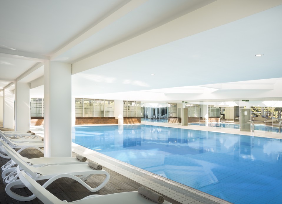Uitzicht op het binnenzwembad, ligstoelen met handdoeken en uitzicht op het groen buiten.