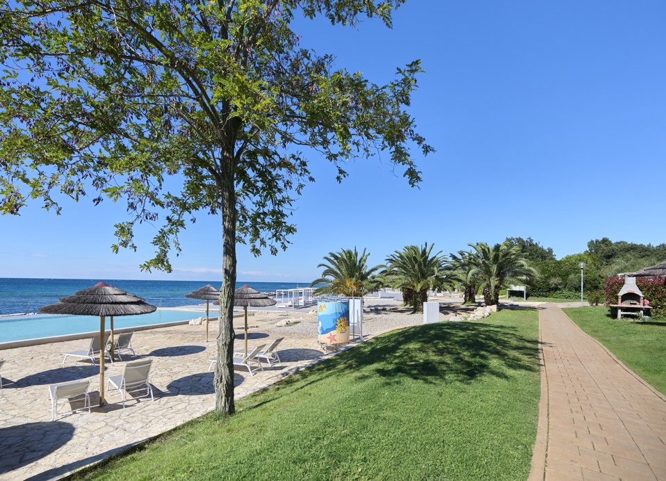 Promenade langs het strand bij Aminess Planet Camping Maravea Resort, omgeven door groen, perfect voor een ontspannen wandeling