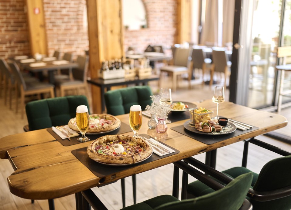 Restaurant table at Aminess Kadoor Hotel with pizzas, grilled dish and beer.