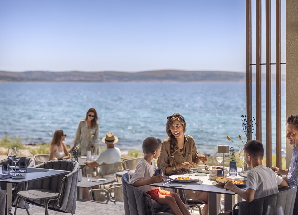 Gezin dineert op een restaurantterras met zeezicht in Avalona Resort
