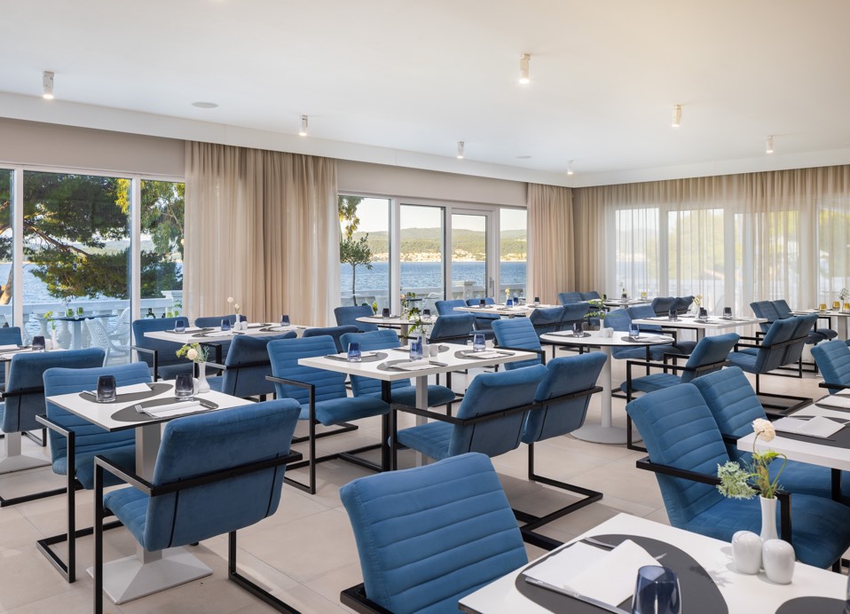 Unico restaurant at Younique Bellevue Hotel with blue chairs and a sea view.