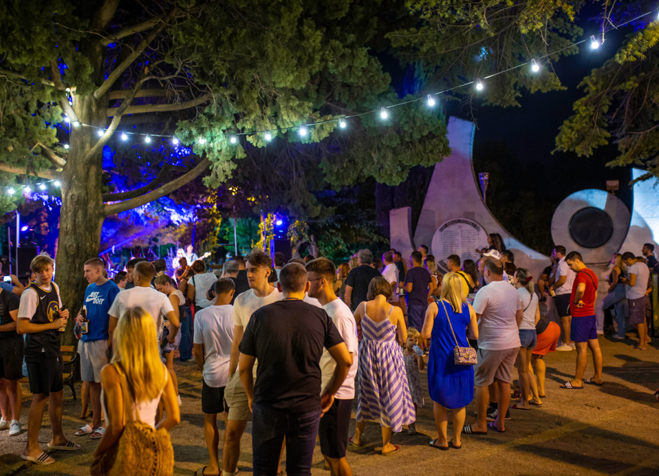 Živahna večerna scena na prostem z lučkami na vrvici, glasbo in množico, ki uživa v prazničnem vzdušju pri La Gradelanear Aminess Style Camping Atea Resort.