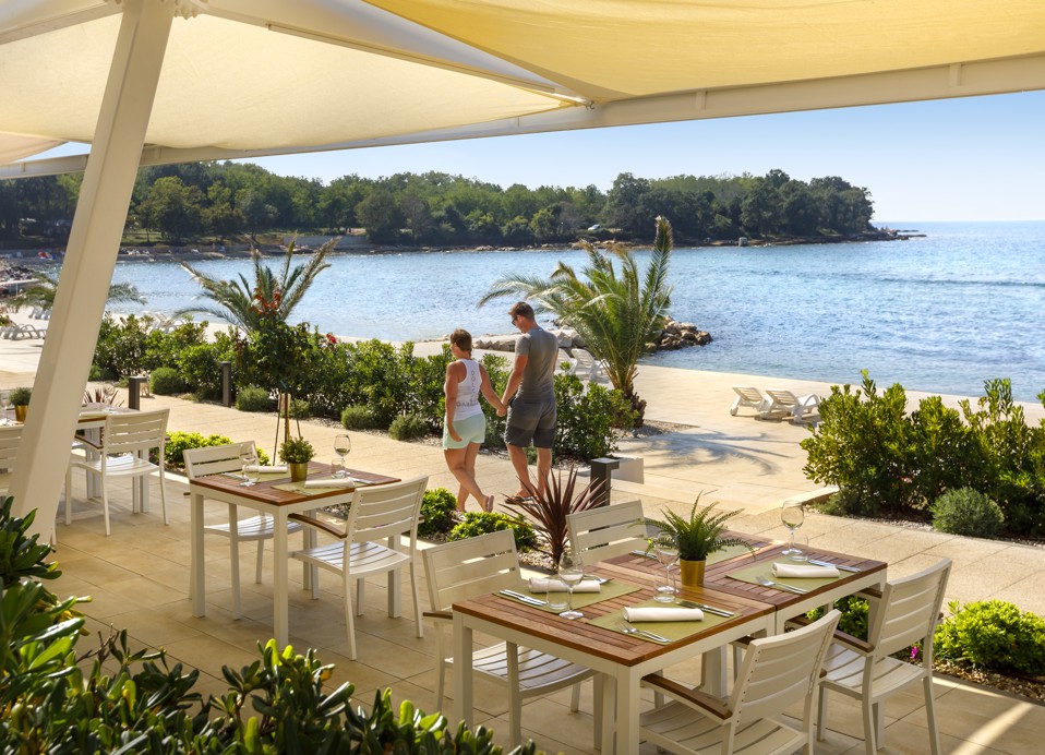 Paar spaziert neben der Terrasse des Restaurants Capa im Aminess Planet Camping Maravea Resort, Novigrad Kroatien